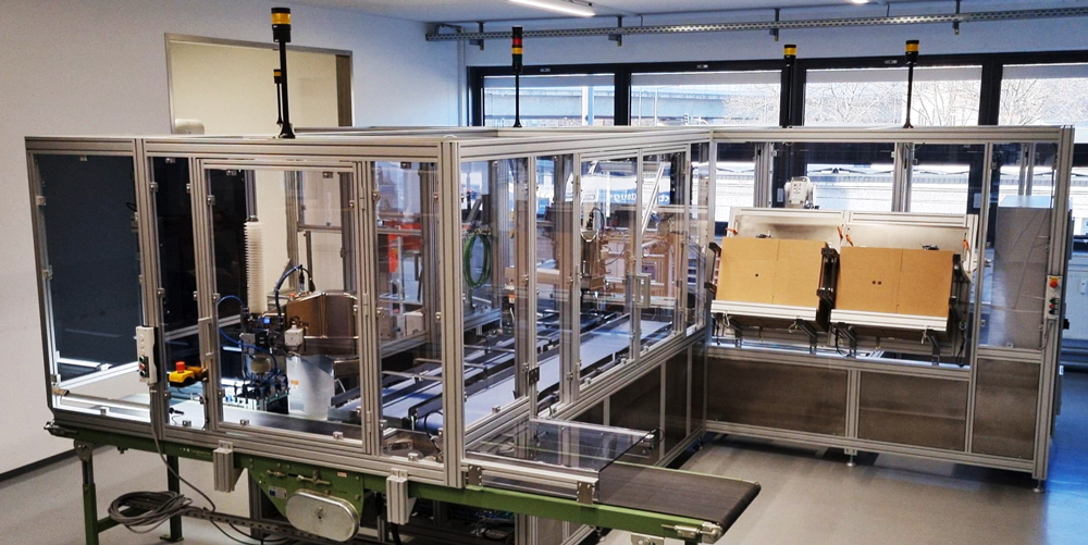 Automatisierte-verpackungsanlage-fuer-maximale-flexibilitaet-item-blog-bild-im-beitrag-1 Sistema de embalaje y paletizado con cintas transportadoras, cerramiento y estaciones de robots